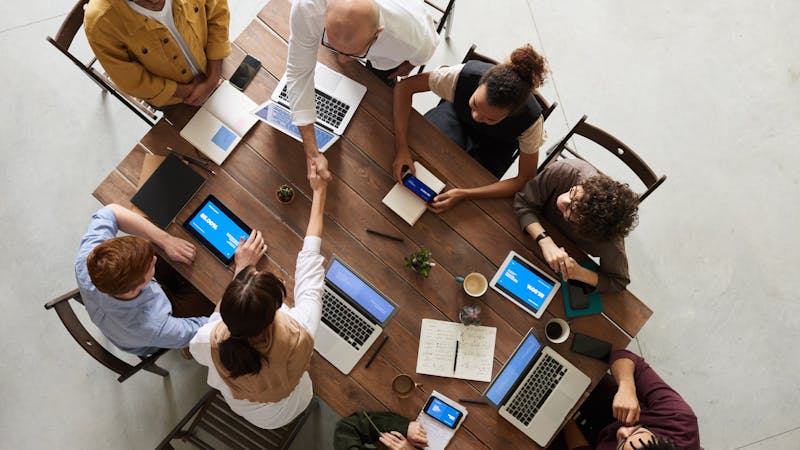 Team an einem Tisch beim Handschlag als Sinnbild für erfolgreiche Leadgenerierung und neue Kundenbeziehungen